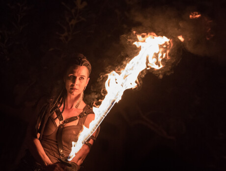 Person dressed as warrior holding a flaming sword at night