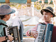 Two young people dressed in traditional Trentino attire are playing in the town band among the tables of the village festival.