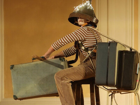 L'immagine mostra la protagonista durante lo spettacolo mentre è in partenza con le sue valigie, un imbuto in testa e delle lucine sopra