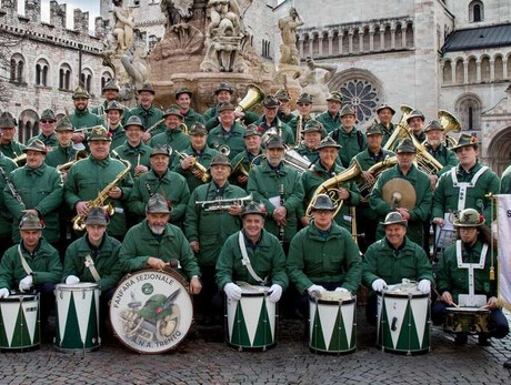 L'immagine mostra i componenti della Fanfara sezione ANA di Trento in posa sotto la fontana del Nettuno, in piazza Duomo a Trento