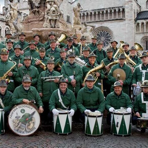 L'immagine mostra i componenti della Fanfara sezione ANA di Trento in posa sotto la fontana del Nettuno, in piazza Duomo a Trento