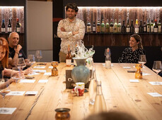 A group of people are seated at a table in the tasting room of a winery. They are enjoying themselves together with the winemaker, who is leading the tasting of his wines.